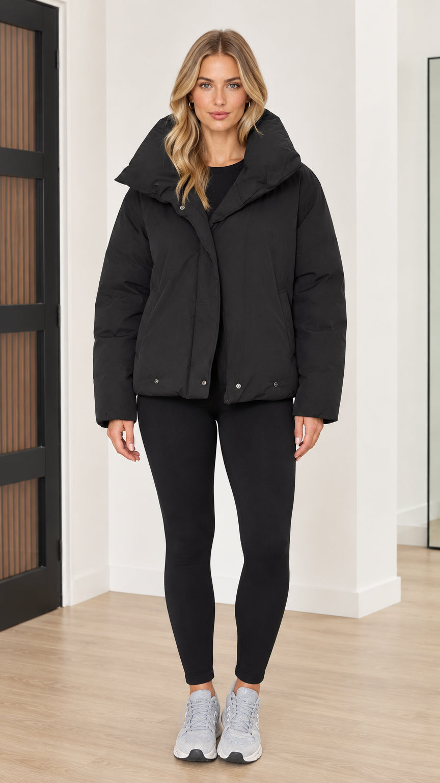 Front full view of woman wearing black oversized funnel collar puffer jacket with black leggings