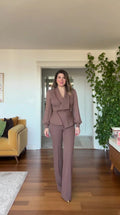 Front full-length view of woman wearing mauve beaded lapel asymmetric blazer and wide leg pants suit set
