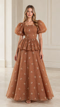Front full view of woman wearing toffee brown floral embroidered puff sleeve peplum maxi gown