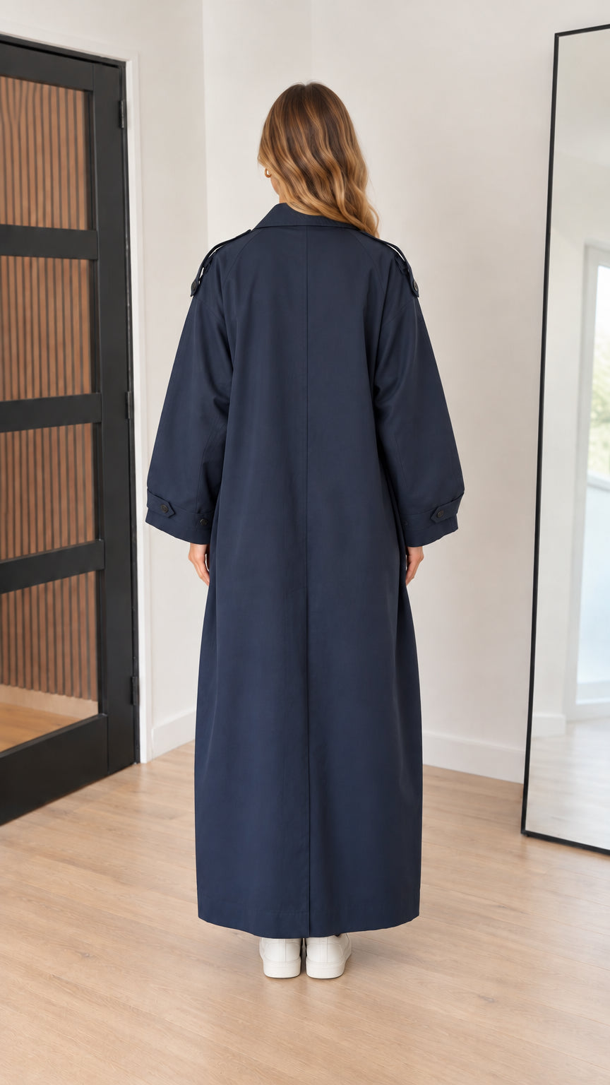 Back view of woman wearing navy blue full-length trench coat with back vent